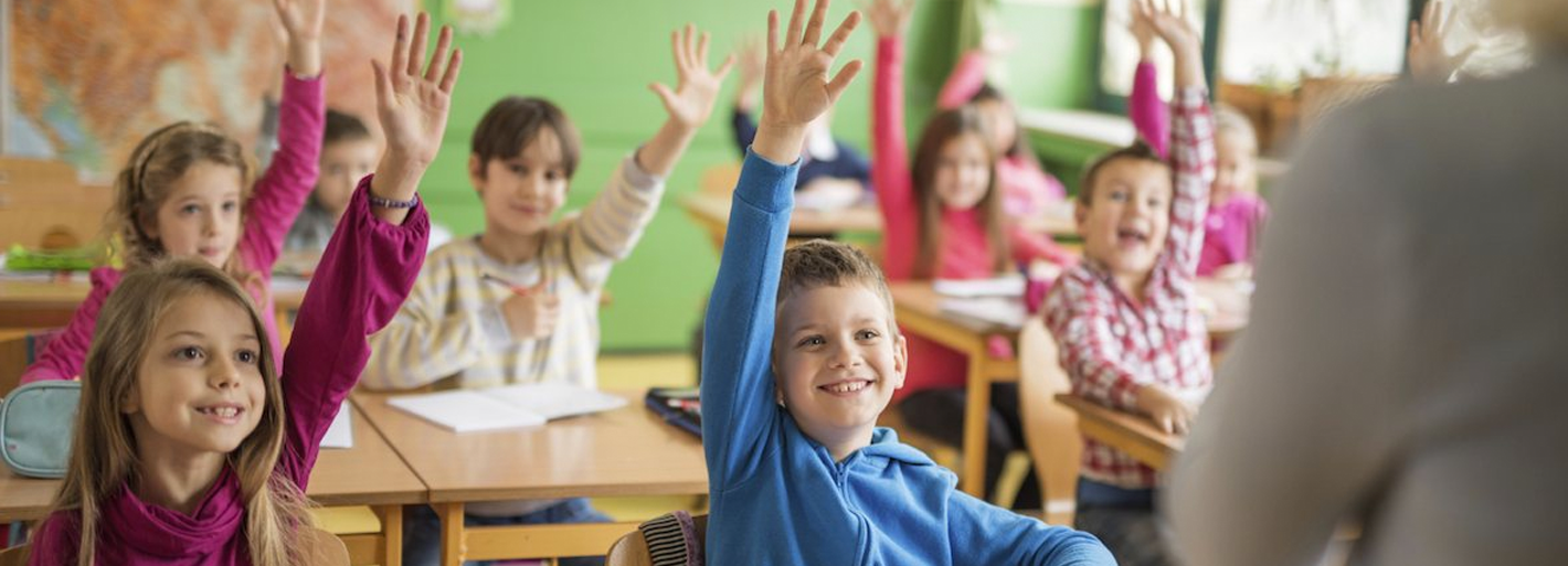 Basisschoolleerlingen steken enthousiast hun hand op tijdens de les.